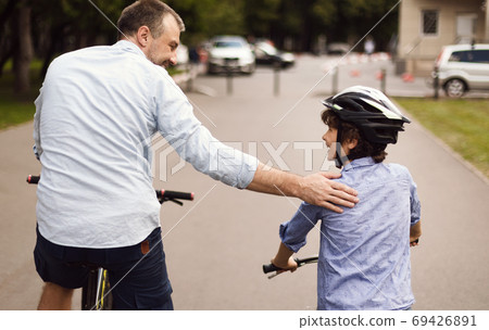 Back view of kid riding bicycle with his happy dad 69426891