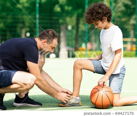 Smiling dad tying shoelaces of his son on playground Smiling dad tying shoelaces of his son on playground 69427170