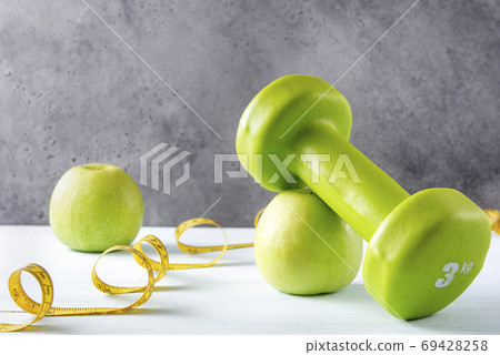 green dumbbell, 2 apples, measuring tape on a green dumbbell, 2 apples, measuring tape on a 69428258