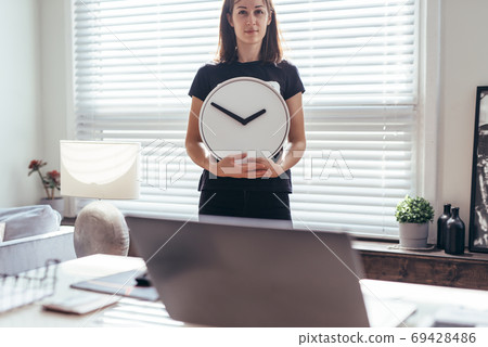 Woman in office with large wall clock. 69428486