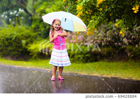 Kid with umbrella playing in summer rain. 69428884