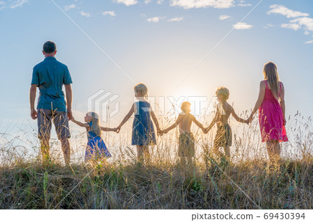 A large family is standing holding hands against the background of the sunset. 69430394
