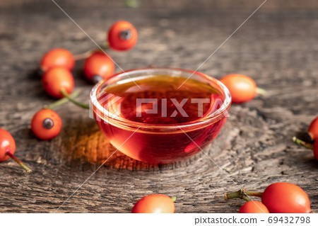 Rose hip seed oil in a bowl, with fresh rose hips 69432798