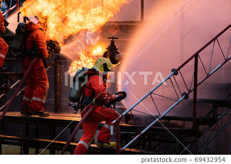 Firefighter team using water fog spraying down fire from oil rig Firefighter team using water fog spraying down fire from oil rig 69432954