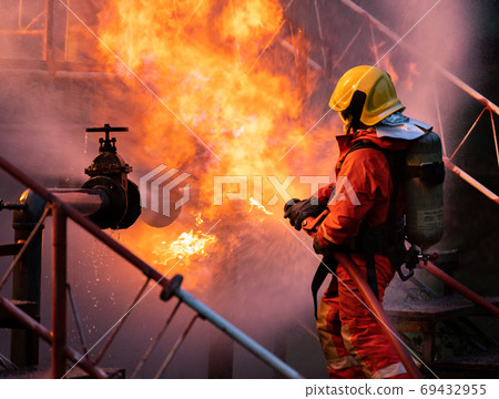Firefighters using water fog spraying down fire from oil rig fac 69432955
