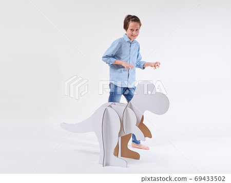 Little dreamer boy playing with a cardboard dinosaur Tyrannosaurus rex. Childhood. Fantasy, imagination. Little dreamer boy playing with a cardboard dinosaur Tyrannosaurus rex. Childhood. Fantasy, imagination. 69433502