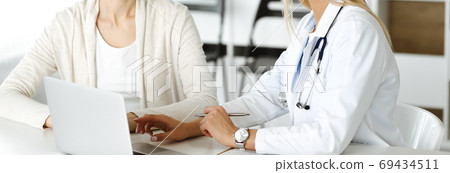 Unknown woman-doctor sitting and communicating with female patient. Physician checks medical history record and exam results, close-up. Healthcare concept 69434511