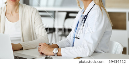Unknown woman-doctor sitting and communicating with female patient. Physician checks medical history record and exam results, close-up. Healthcare concept Unknown woman-doctor sitting and communicating with female patient. Physician checks medical history record and exam results, close-up. Healthcare concept 69434512