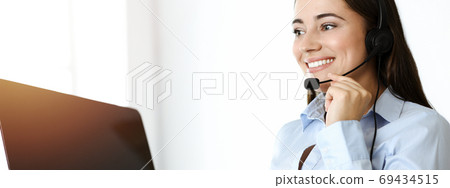 Brunette female customer service representative using headset and consulting clients online. Call center 69434515