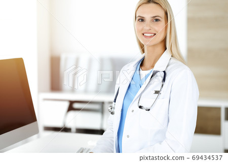 Woman-doctor controls medication history records and exam results while using laptop computer in sunny hospital. Medicine and healthcare concept Woman-doctor controls medication history records and exam results while using laptop computer in sunny hospital. Medicine and healthcare concept 69434537