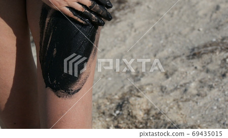 Healing black medical mud applies to leg and knee woman at the lake of salt water. Salty black dirt for people with health and skin problems. Relax at spa resort. Exfoliation scrub beauty treatment Healing black medical mud applies to leg and knee woman at the lake of salt water. Salty black dirt for people with health and skin problems. Relax at spa resort. Exfoliation scrub beauty treatment 69435015