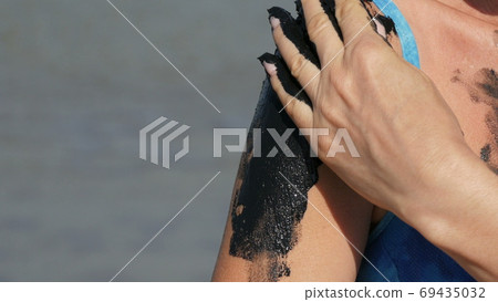 Healing black medical mud applies to arm shoulder woman at the lake of salt water. Salty black dirt for people with health and skin problems. Relax at spa resort. Exfoliation scrub beauty treatment Healing black medical mud applies to arm shoulder woman at the lake of salt water. Salty black dirt for people with health and skin problems. Relax at spa resort. Exfoliation scrub beauty treatment 69435032