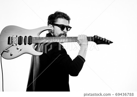 A man holds a guitar in his hands black leather jacket dark glasses music performance light background A man holds a guitar in his hands black leather jacket dark glasses music performance light background 69436788