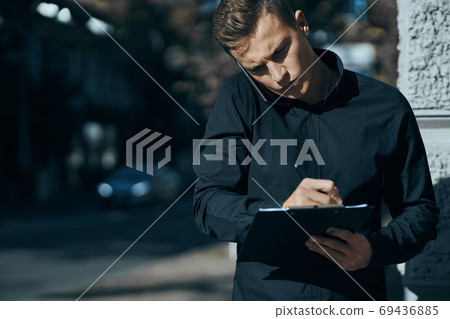 Business man in a shirt near the building with documents in his hands Business man in a shirt near the building with documents in his hands 69436885