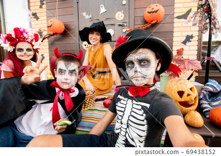 Two boys and girl with painted faces sitting on background of happy young woman 69438152