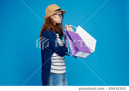 fashionable woman is shopping with packages on a blue background in a striped t-shirt and jacket, glasses on her face 69438363