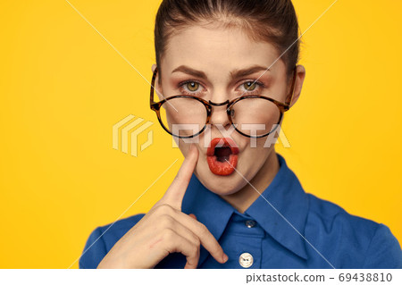 A woman in a blue shirt and glasses with bright makeup on her face is gesturing with her hands Copy Space A woman in a blue shirt and glasses with bright makeup on her face is gesturing with her hands Copy Space 69438810