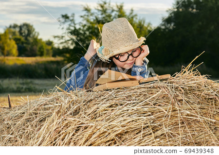 Reading girl sits over the haystack roll on field in countryside 69439348