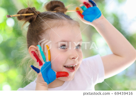 Funny cute little girl with her hands stained in paint. The concept of children's creativity. 69439416
