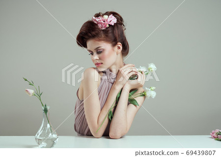 romantic woman with flowers in her hair and vase with pink flower light background table 69439807