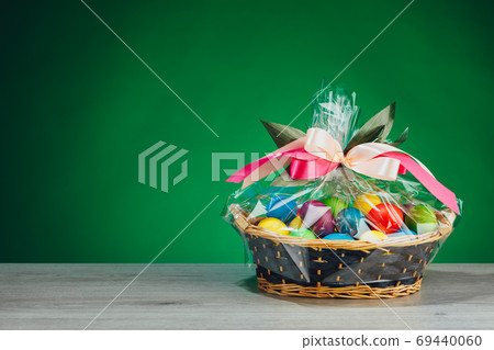 Easter gift basket with multicolor eggs, green background 69440060