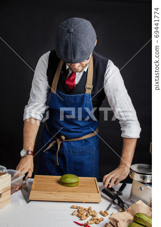 Cook stands in the studio near a wooden table against black wall. Cook stands in the studio near a wooden table against black wall. 69441774