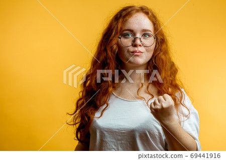 Young pretty ginger woman shows fist, with angry or aggressive expression Young pretty ginger woman shows fist, with angry or aggressive expression 69441916