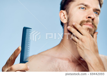 A man with a comb in his hands caring for a beard bare shoulders  69442093