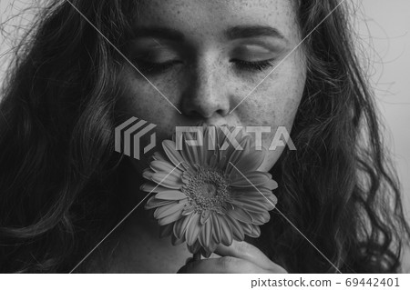 Close up of beautiful redhead woman smelling flower over yellow background Close up of beautiful redhead woman smelling flower over yellow background 69442401