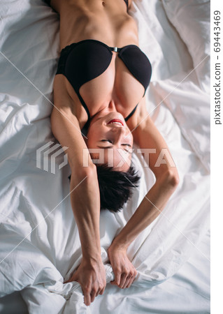 Brunette model female in bed. Top view of beautiful young woman in black lingerie lying in bed 69443469