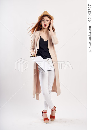 woman with a folder of documents on a light background in sandals and in a pink coat gesturing with her hands emotions woman with a folder of documents on a light background in sandals and in a pink coat gesturing with her hands emotions 69443707