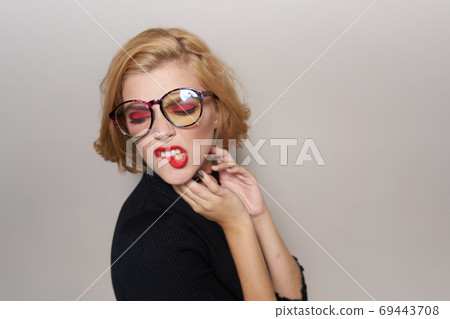 Blonde with short hairstyle with glasses red lips black jacket light background cropped view Blonde with short hairstyle with glasses red lips black jacket light background cropped view 69443708
