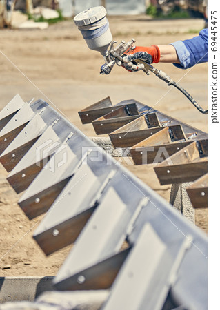 Crop man painting metal detail with paint gun in the backyard 69445475