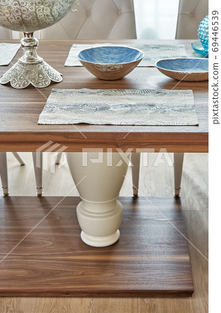 Wooden dinner table on massive legs with dishware in modern apartment. Close-up Wooden dinner table on massive legs with dishware in modern apartment. Close-up 69446539