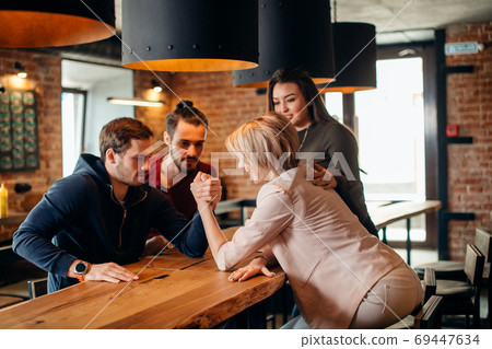 Cheerful gyu and girl having fun arm wrestling each other in pub. Cheerful gyu and girl having fun arm wrestling each other in pub. 69447634