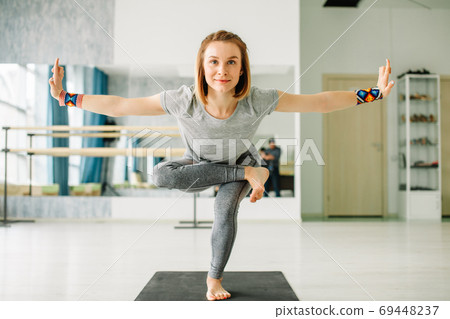 Woman doing balancing exercises during a yoga workout in well lit gym Woman doing balancing exercises during a yoga workout in well lit gym 69448237