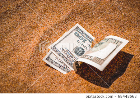 Money dolars half covered with sand lie on beach close-up Money dolars half covered with sand lie on beach close-up 69448668