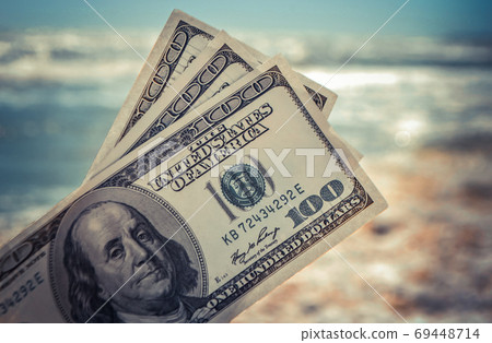 Girl holding money bill of 300 dollars on background of sea ocean Girl holding money bill of 300 dollars on background of sea ocean 69448714