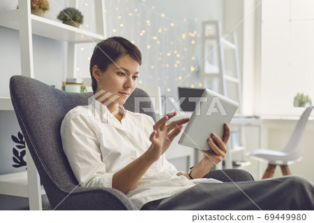 Casual female manager working on tablet sitting in a chair in her office. Casual female manager working on tablet sitting in a chair in her office. 69449980