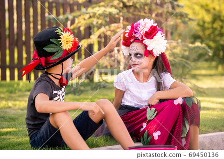 Cute boy in hat and t-shirt touching floral wreath on head of pretty girl 69450136