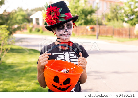Boy with painted face in black halloween t-shirt and elegant hat holding treats 69450151
