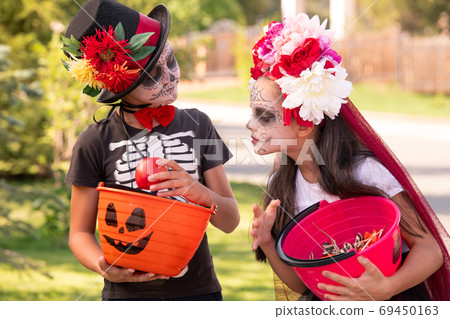 Cute halloweeen girl with dark long hair looking at friend basket with treats 69450163