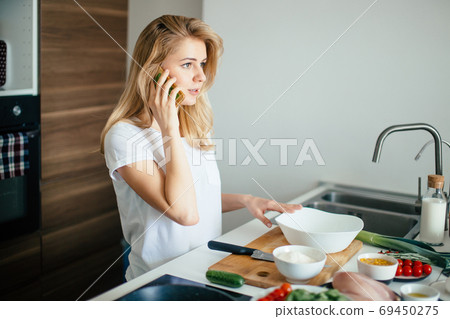 Caucasian woman making healthy meal and reading message at phone in kitchen. Caucasian woman making healthy meal and reading message at phone in kitchen. 69450275