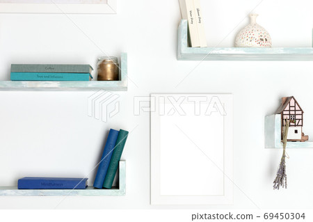 Poster mockup. A blank frame for a drawing on a wall with books and objects Poster mockup. A blank frame for a drawing on a wall with books and objects 69450304
