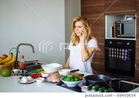 Caucasian woman making healthy meal and reading message at phone in kitchen. Caucasian woman making healthy meal and reading message at phone in kitchen. 69450654