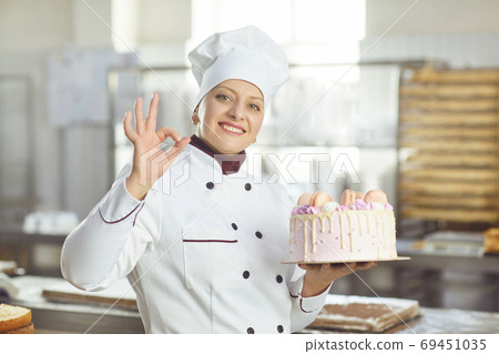 Confectioner is holding a cake in her hand in the bakery. 69451035