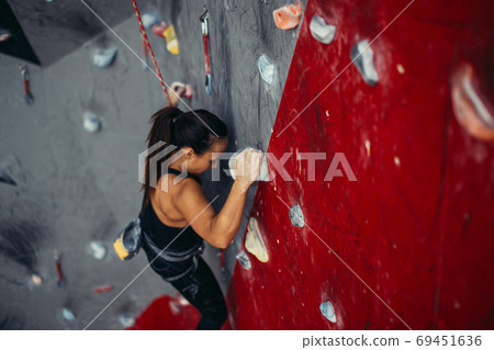 Beautiful young strong woman climbing on red artificial wall top view. Beautiful young strong woman climbing on red artificial wall top view. 69451636