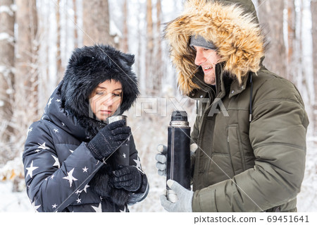 Young couple in love drink a hot drink from a thermos and enjoy winter nature. Young couple in love drink a hot drink from a thermos and enjoy winter nature. 69451641