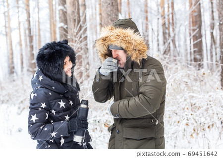 Season and walk concept - Happy couple drinking hot tea in winter forest Season and walk concept - Happy couple drinking hot tea in winter forest 69451642