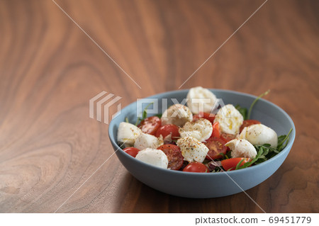 Salad with mozxarella, tomatoes and arugula in a blue bowl on walnut wood table 69451779